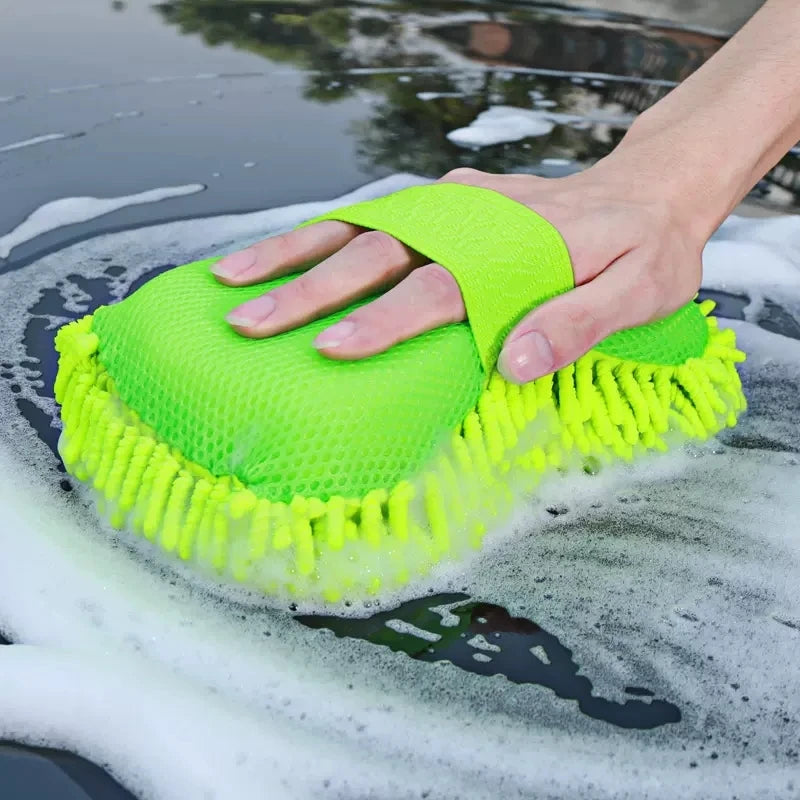 Hand using a green car wash scrubber on a soapy surface