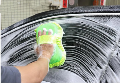 Person cleaning a car window with a green sponge in a garage setting