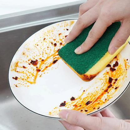 Person cleaning a plate with a green sponge in a sink