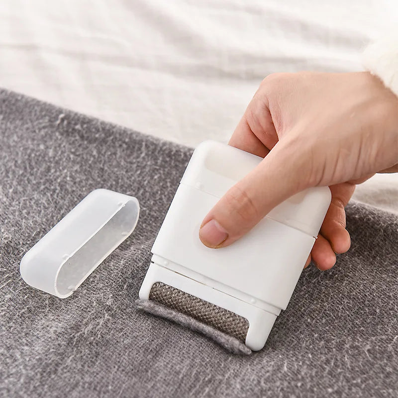 White fabric defuzzer being used on a piece of gray fabric with a hand holding it.