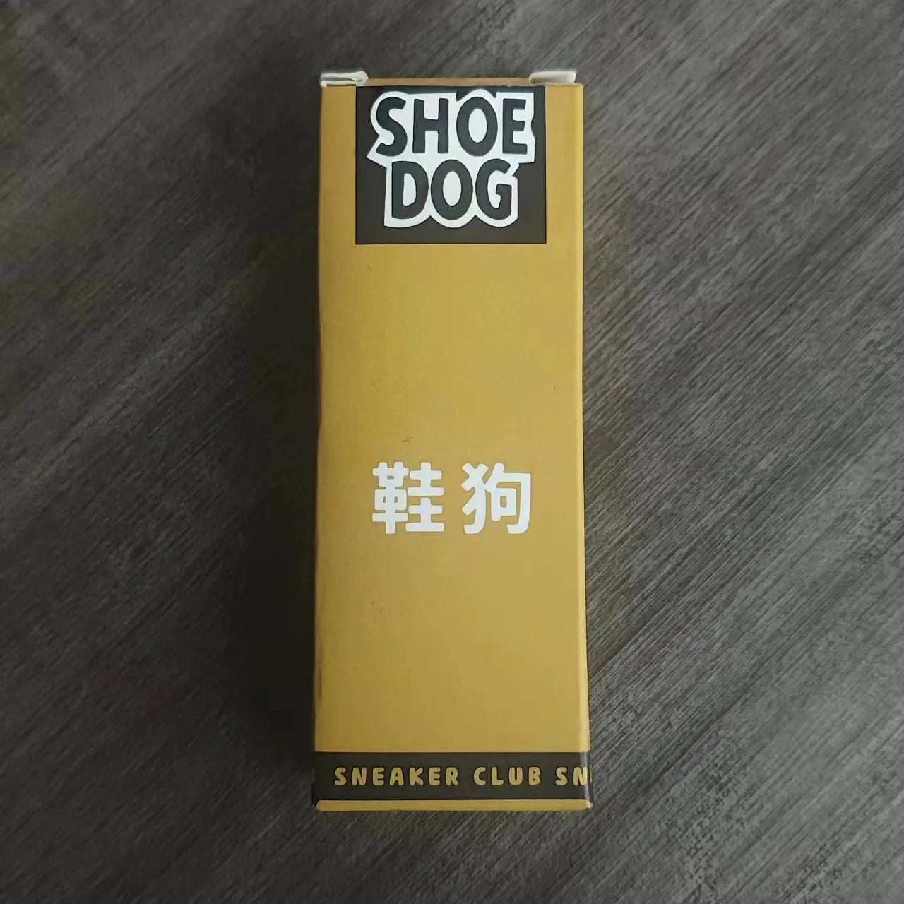 Gold box with 'Shoe Dog' branding on a dark wooden surface
