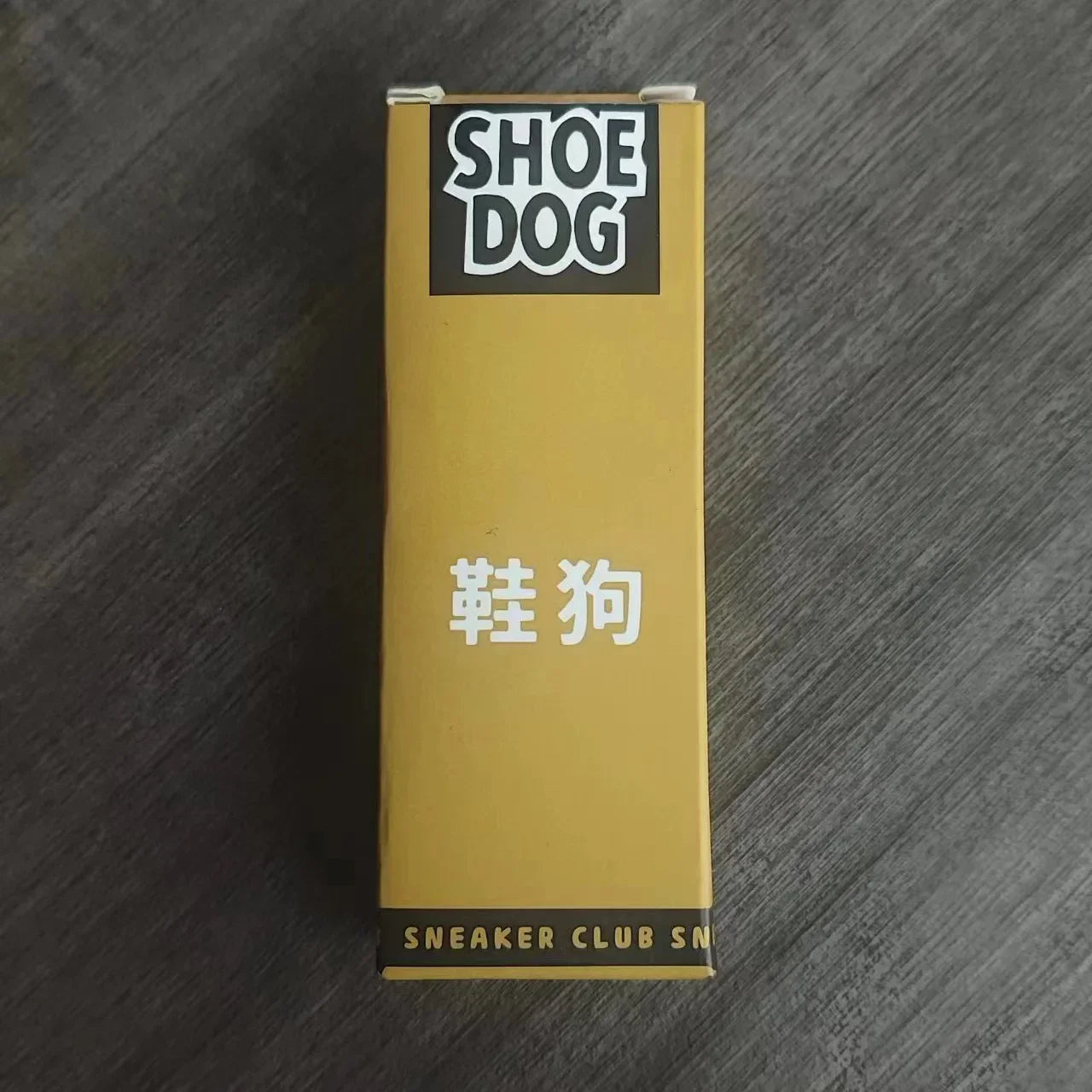 Gold box with 'Shoe Dog' branding on a dark wooden surface